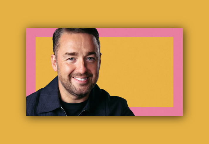 Person wearing a dark collared jacket against a vibrant background featuring a large yellow rectangle centered on a pink backdrop. The composition is simple and modern, with bold contrasting colours creating a striking visual effect.