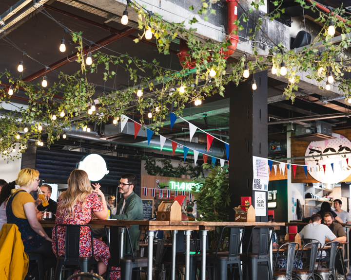 Inside the foodhall Sheffield Plate. Lots of people are sat at table eating and drinking.