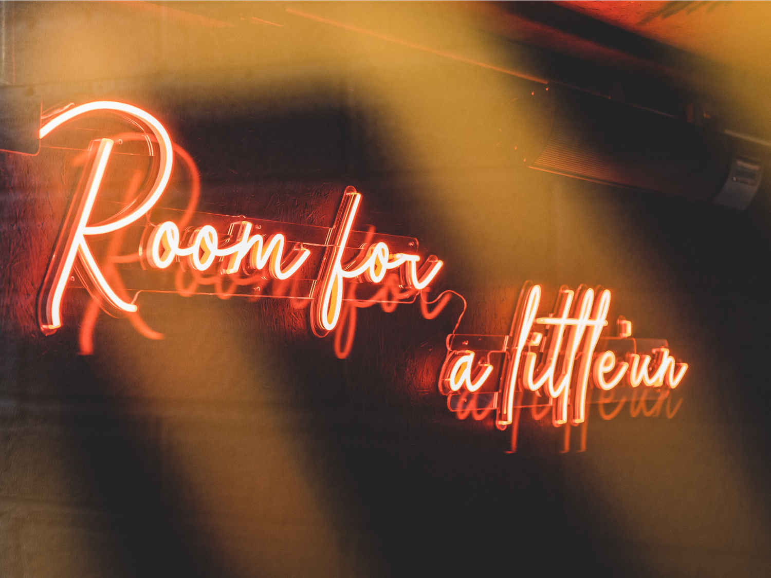 Red neon sign on a wall at Nook that reads 'Room for a little'un'