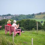 A couple sat on a pink bench on top of a hill.