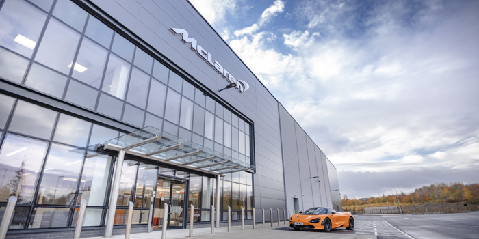An orange McLaren car parked outside the glass McLaren building at The Advanced Manufacturing Innovation District.