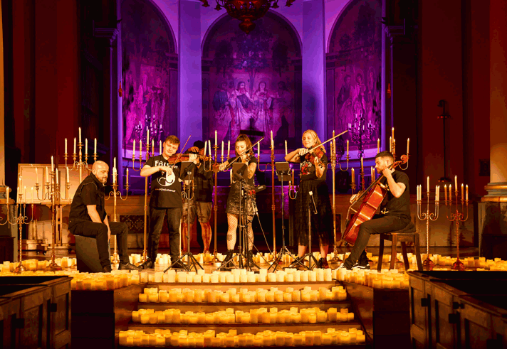 A five piece band perform on a stage, surrounded by candles. 