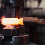 A piece of white-hot metal being shaped in a huge hammer press.