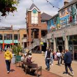 Lots of people are walking about in Orchard Square on a sunny day.