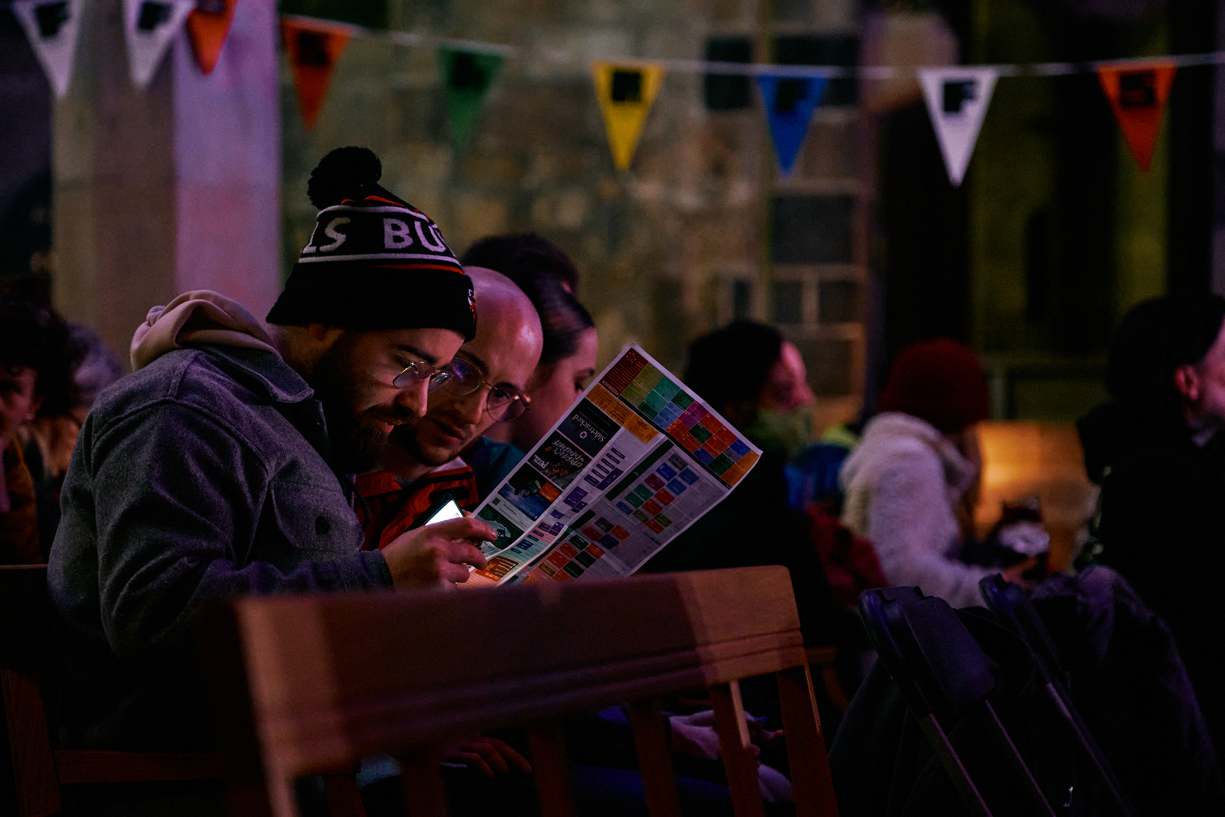 Two men sat down next to eachother reading the events programme for Sheffield Adventure Film Festival