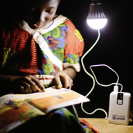 A child reads a story book, lit by a single bulb.