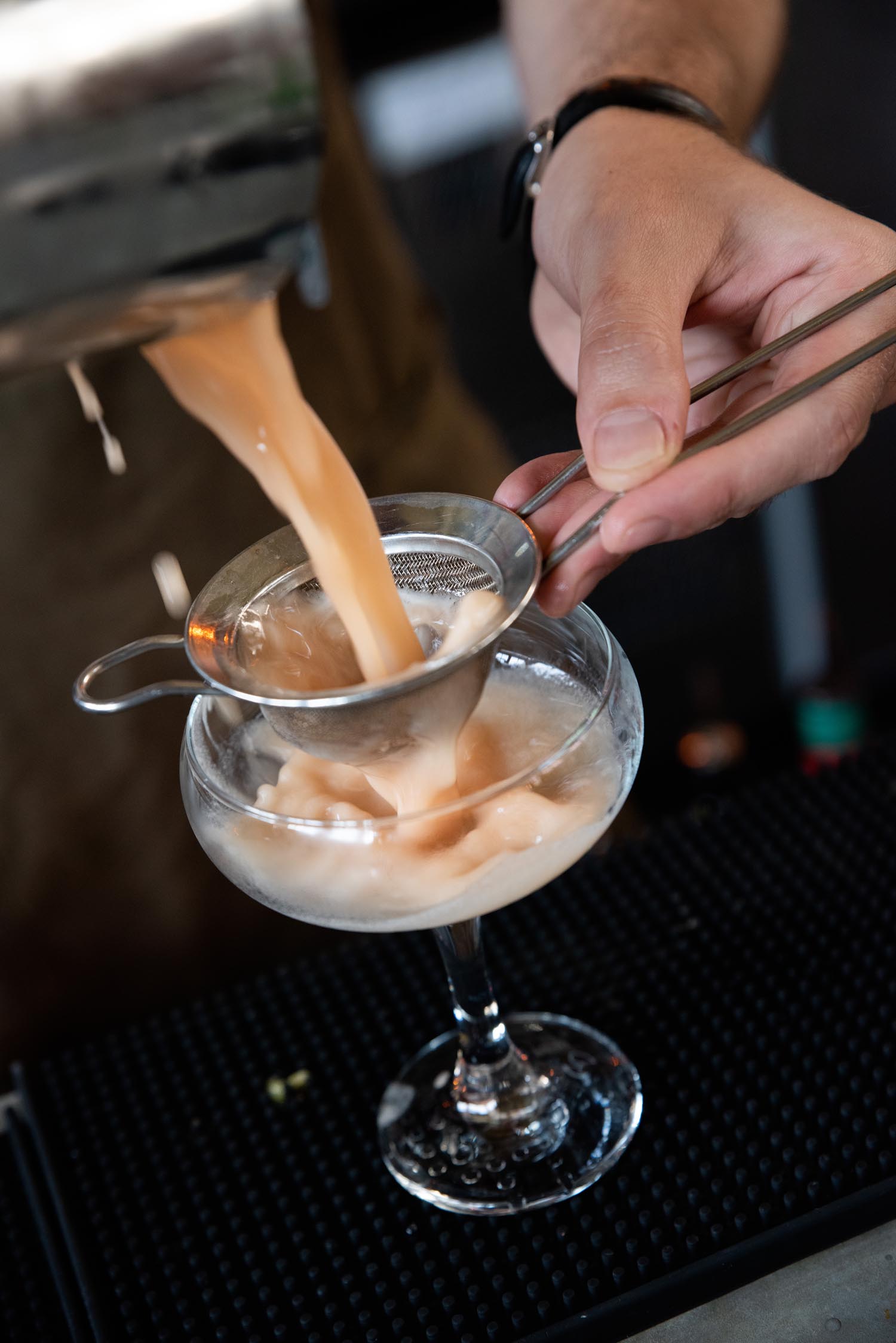 A close-up of a cocktail being poured through a sieve into a glass.