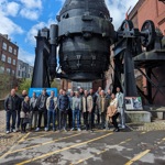 A group of people standing under the Bessemer Converter at Kelham Island. 