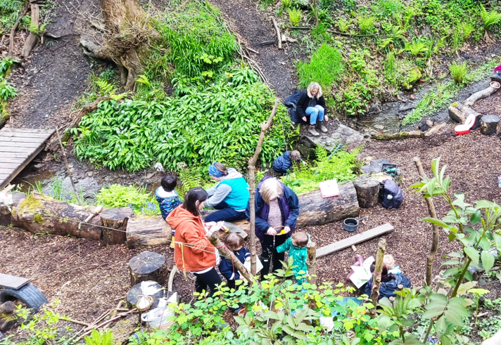 A group of people in a woodland clearing are taking part in a workshop.