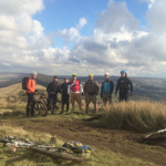 A group of people in the countryside. There are bikes lying on the ground all around the group.