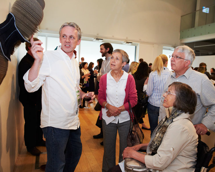 A busy and crowded room full of people looking at artworks that are displayed on the walls.