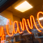 An orange neon sign that reads 'Holy Cannoli'.
