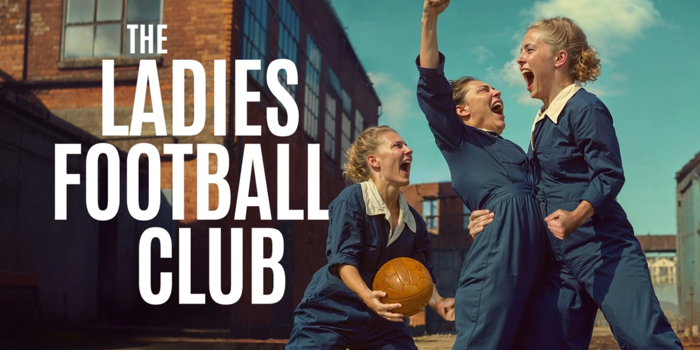 In the courtyard of a factory, three people wearing blue boiler suits scream with joy and triumph. One holds a brown leather ball, one punches the air and one grabs the other's waist. Text reads: THE LADIES FOOTBALL CLUB