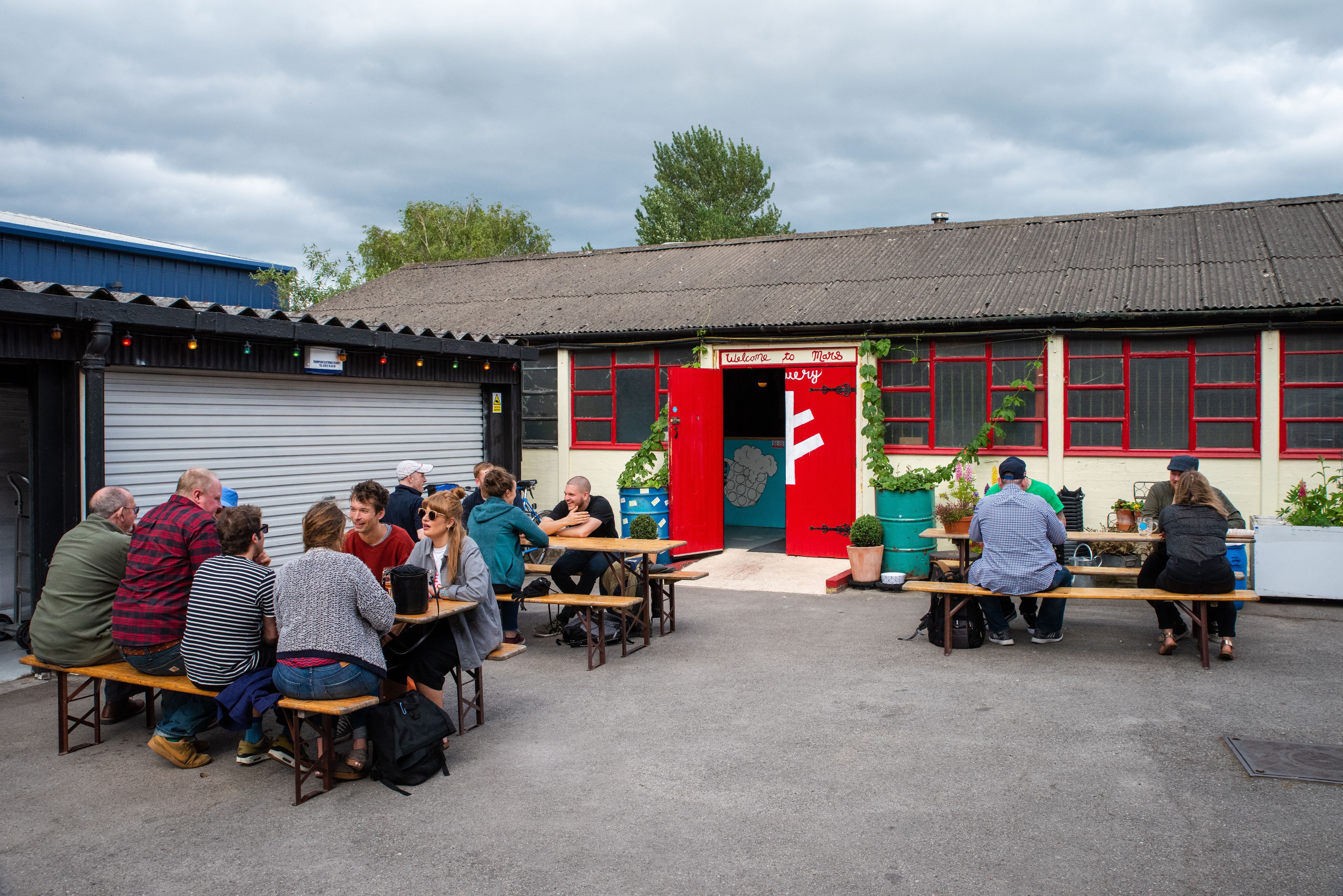 Three benches of people sat outside of Saint Mars of the Desert Taproom on a cloudy day
