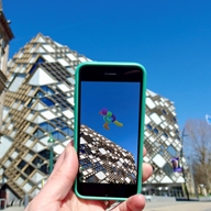 Hand with mobile phone held up in front of The Diamond Building, Sheffield, showing  Look Up AR art