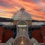 The Meadowhall exterior at sunset, featuring the glass-domed main entrance, red-brick walls and a dramatic orange and pink sky.