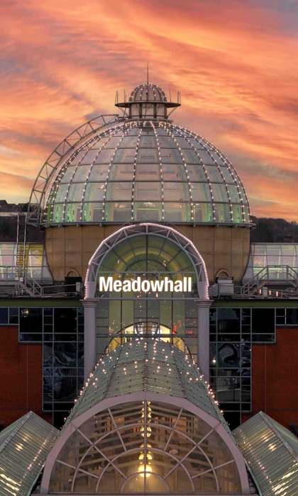 The Meadowhall exterior at sunset, featuring the glass-domed main entrance, red-brick walls and a dramatic orange and pink sky.